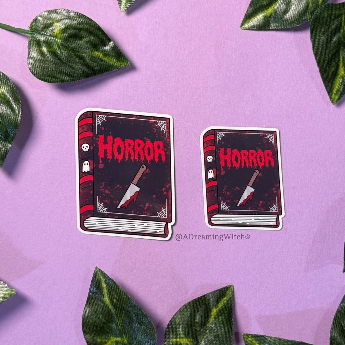 Two 'Horror' book-themed stickers on a purple background with green leaves.