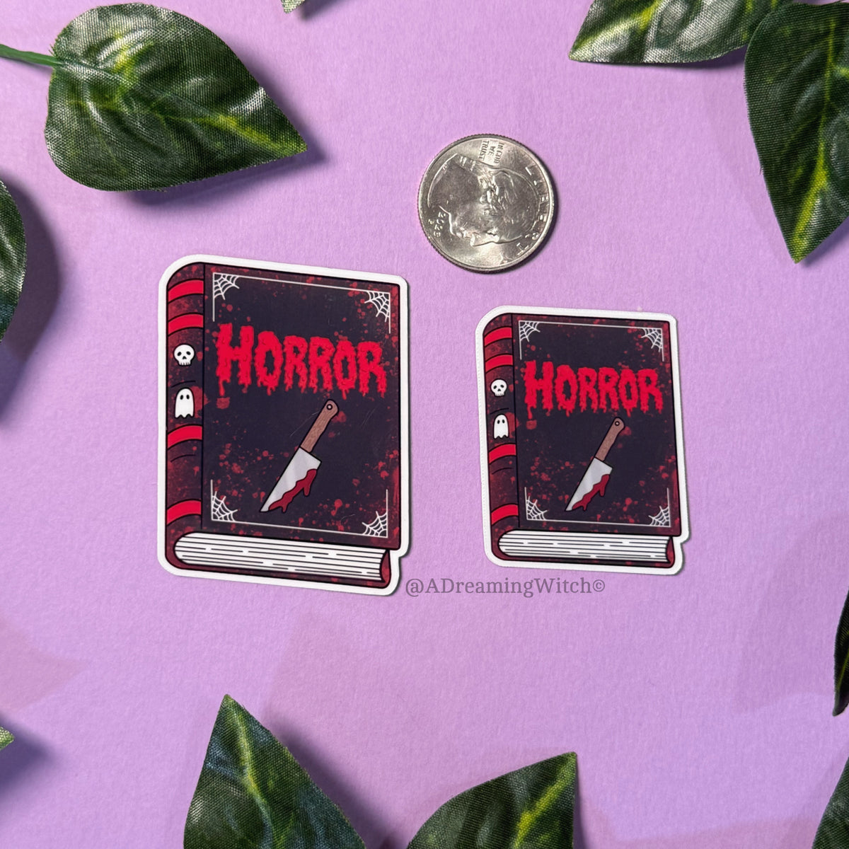 Two 'Horror' book-themed stickers with a quarter for scale on a purple background with leaves.
