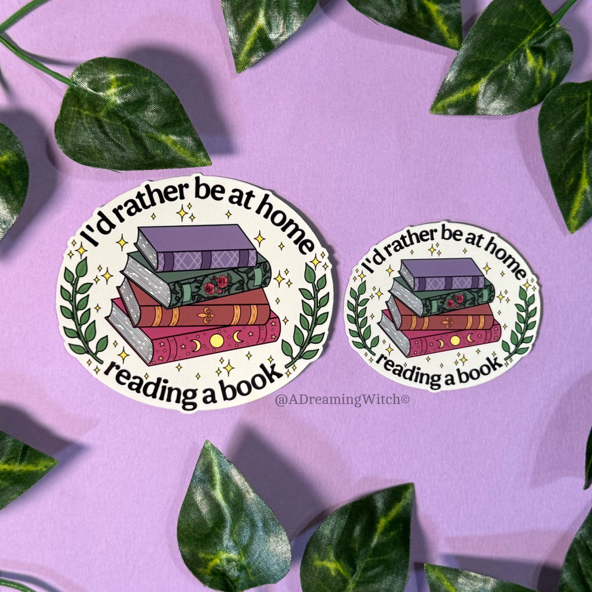 Two stickers with book design and text 'I'd rather be at home reading a book' on a purple background with leaves.