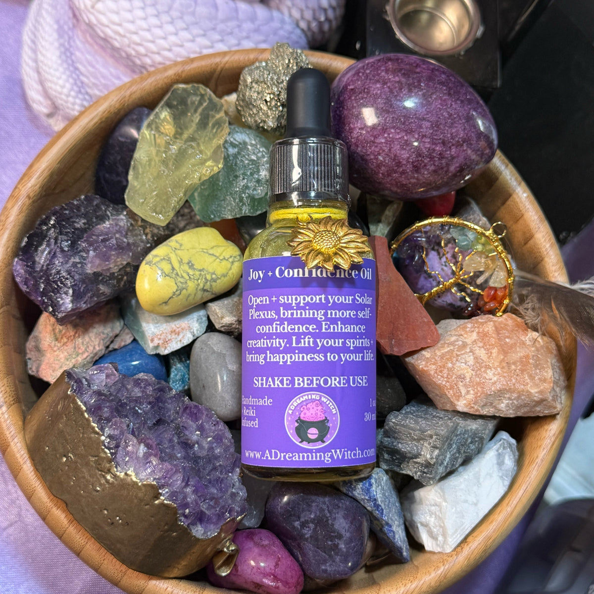 Bottle of joy oil with a purple label surrounded by colorful crystals in a wooden bowl.