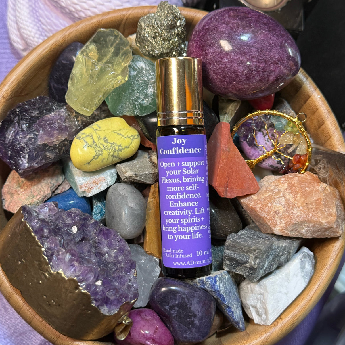 Roll-on bottle labeled 'Joy Confidence' surrounded by colorful crystals in a wooden bowl.