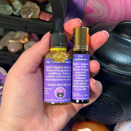 Hand holding two bottles of Joy + confidence oil with purple labels against a mystical background.