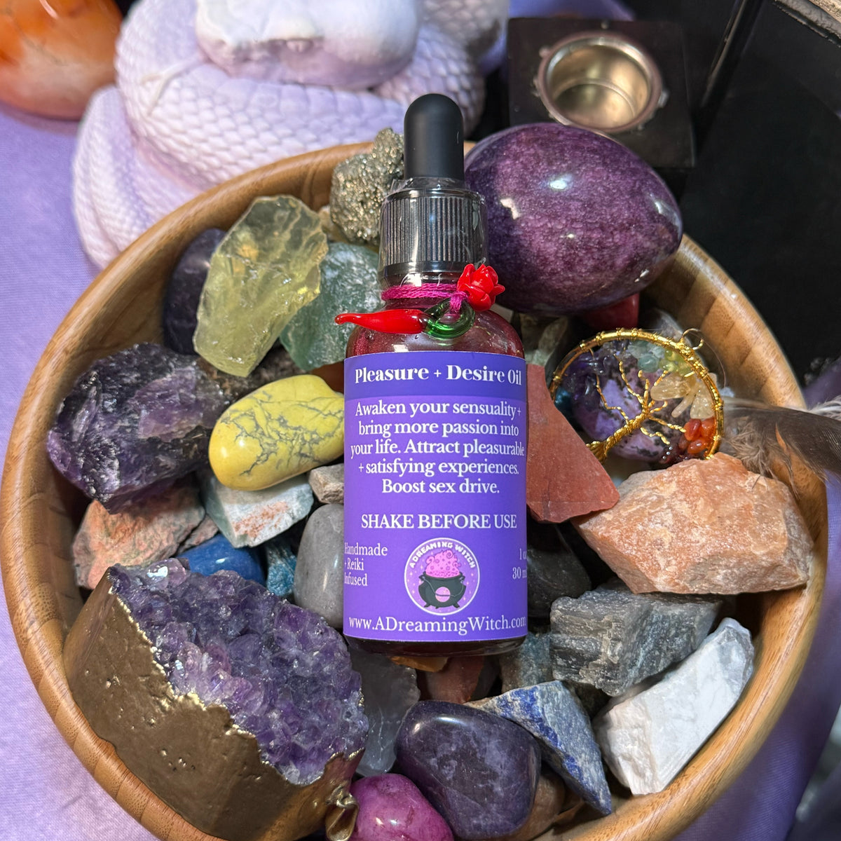Bottle of 'Pleasure + Desire Oil' surrounded by colorful crystals in a wooden bowl.