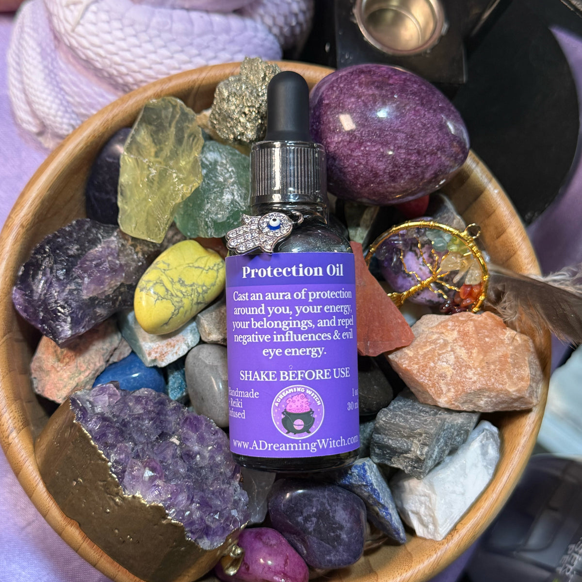 Protection oil bottle with purple label on a bed of colorful crystals in a wooden bowl.