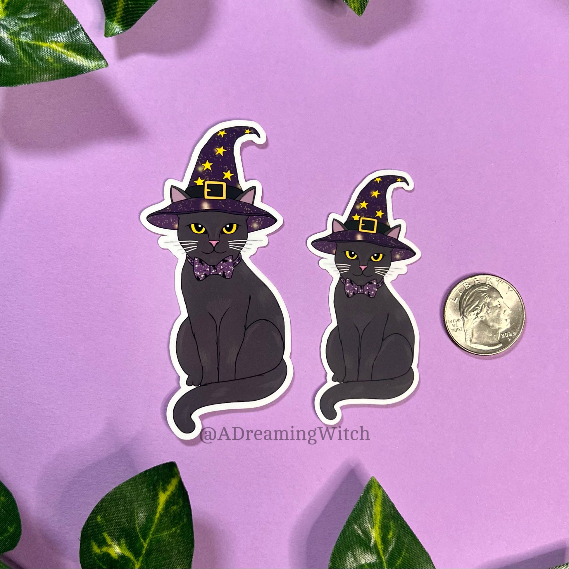 image of 2 stickers of black witchy cats, wearing a purple witch hat with yellow stars and celestial designs, in comparison to a quarter for sizing reference