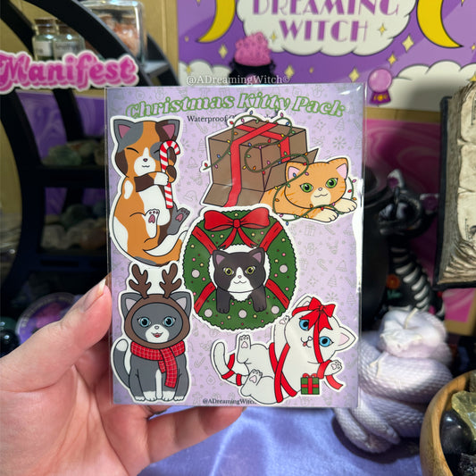 Pack of Christmas-themed cat stickers held by a hand with a colorful background.
