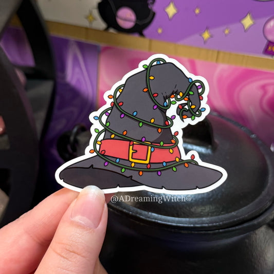 Sticker of a witch hat with lights held by a hand against a colorful background.