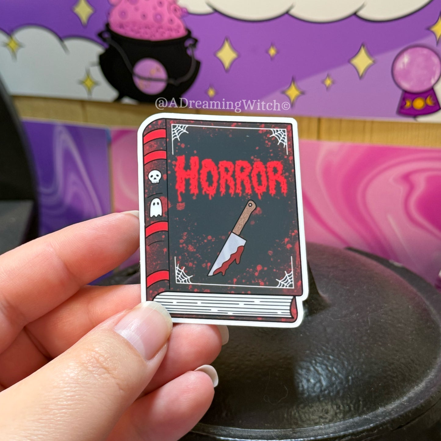 book sticker with 'Horror' text and knife illustration held by a hand, with a colorful background.