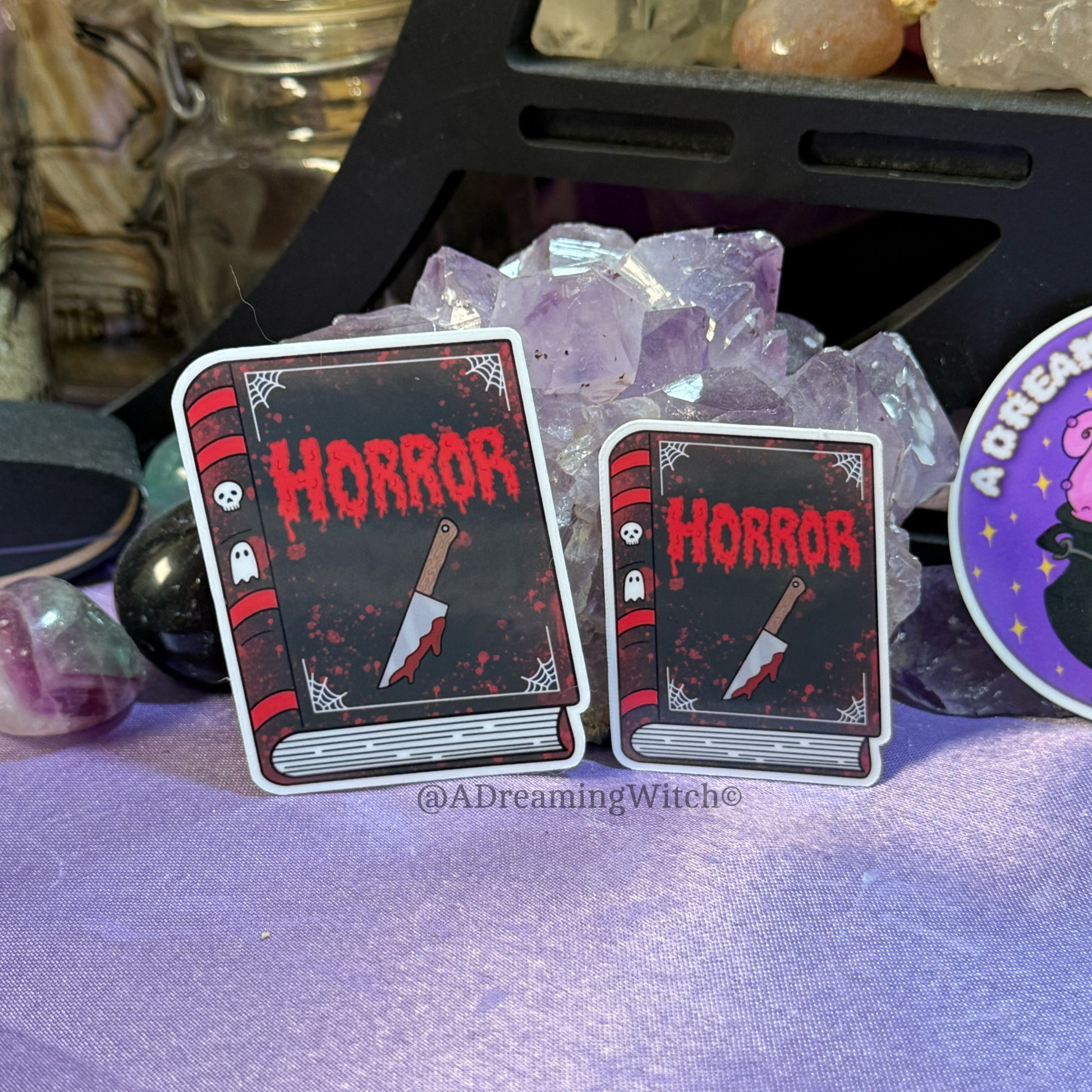 Two horror-themed book stickers with a knife and ghost design on a purple surface.