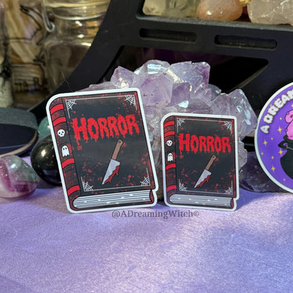 Two horror-themed book stickers with a knife and ghost design on a purple surface.