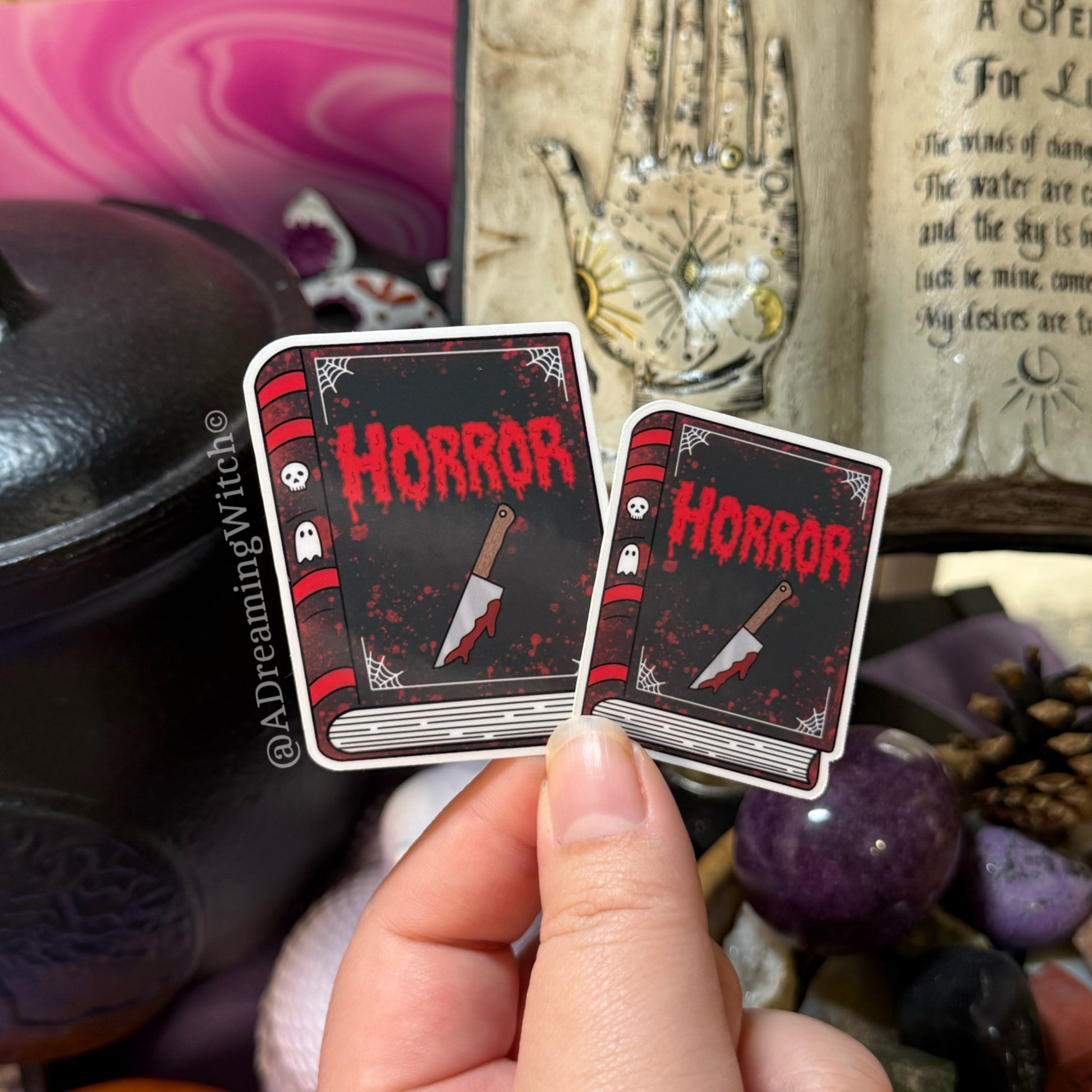 Two 'Horror' themed book stickers held by a hand with mystical background elements.