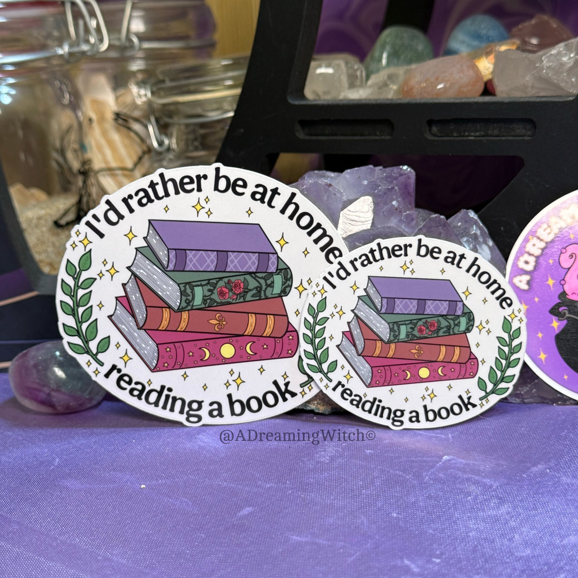 Two stickers with a book-themed design on a purple surface with crystals in the background.