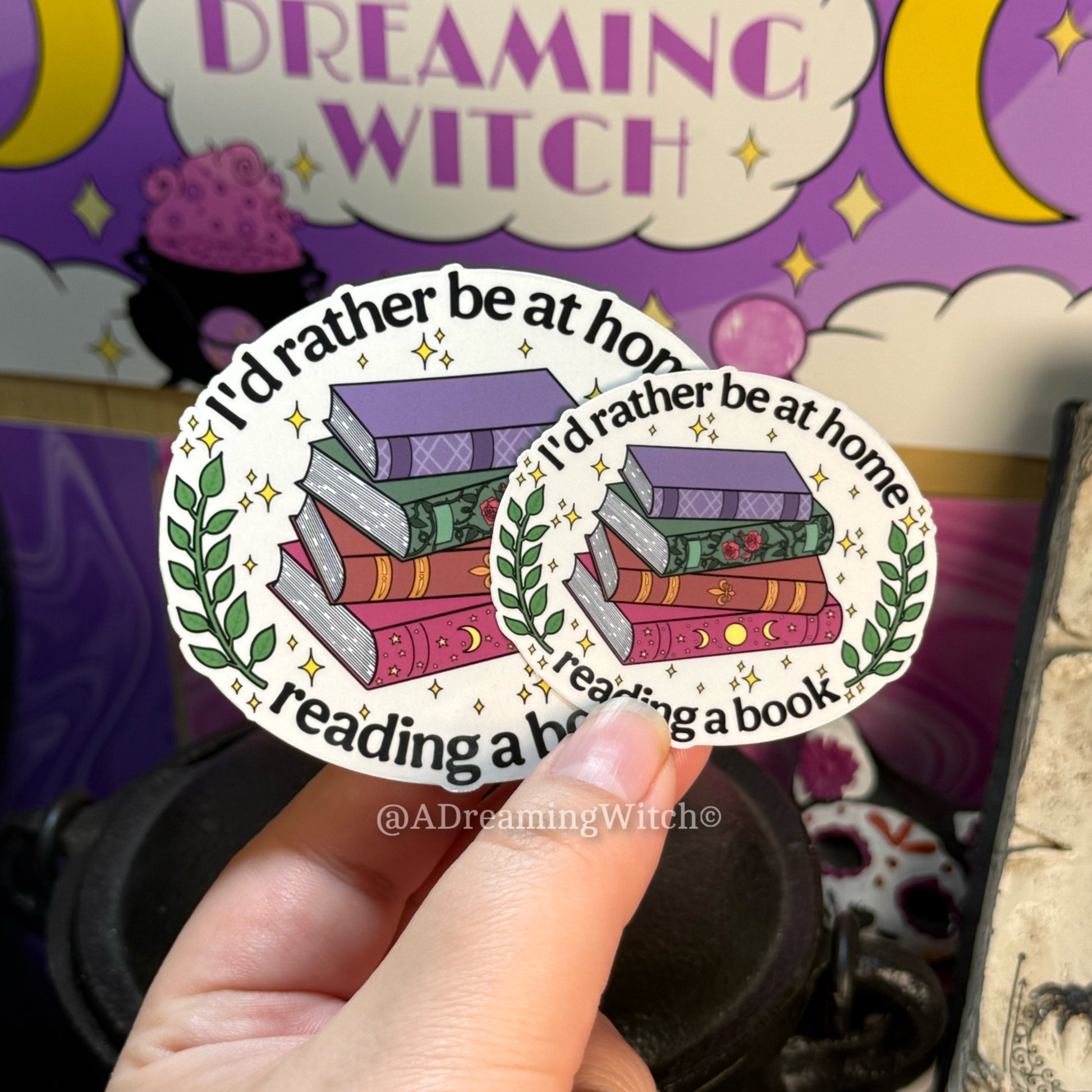 Two stickers with a book design held by a hand against a colorful background.