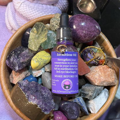 Intuition oil bottle surrounded by colorful crystals in a wooden bowl.