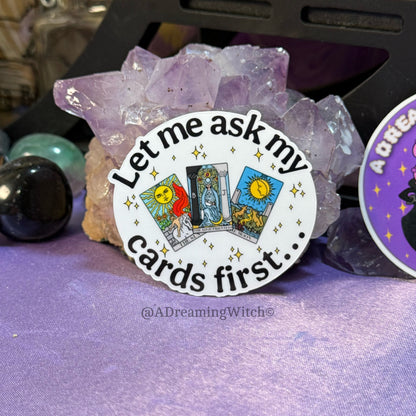 Sticker with tarot card design and text 'Let me ask my cards first' on a purple background with crystals.