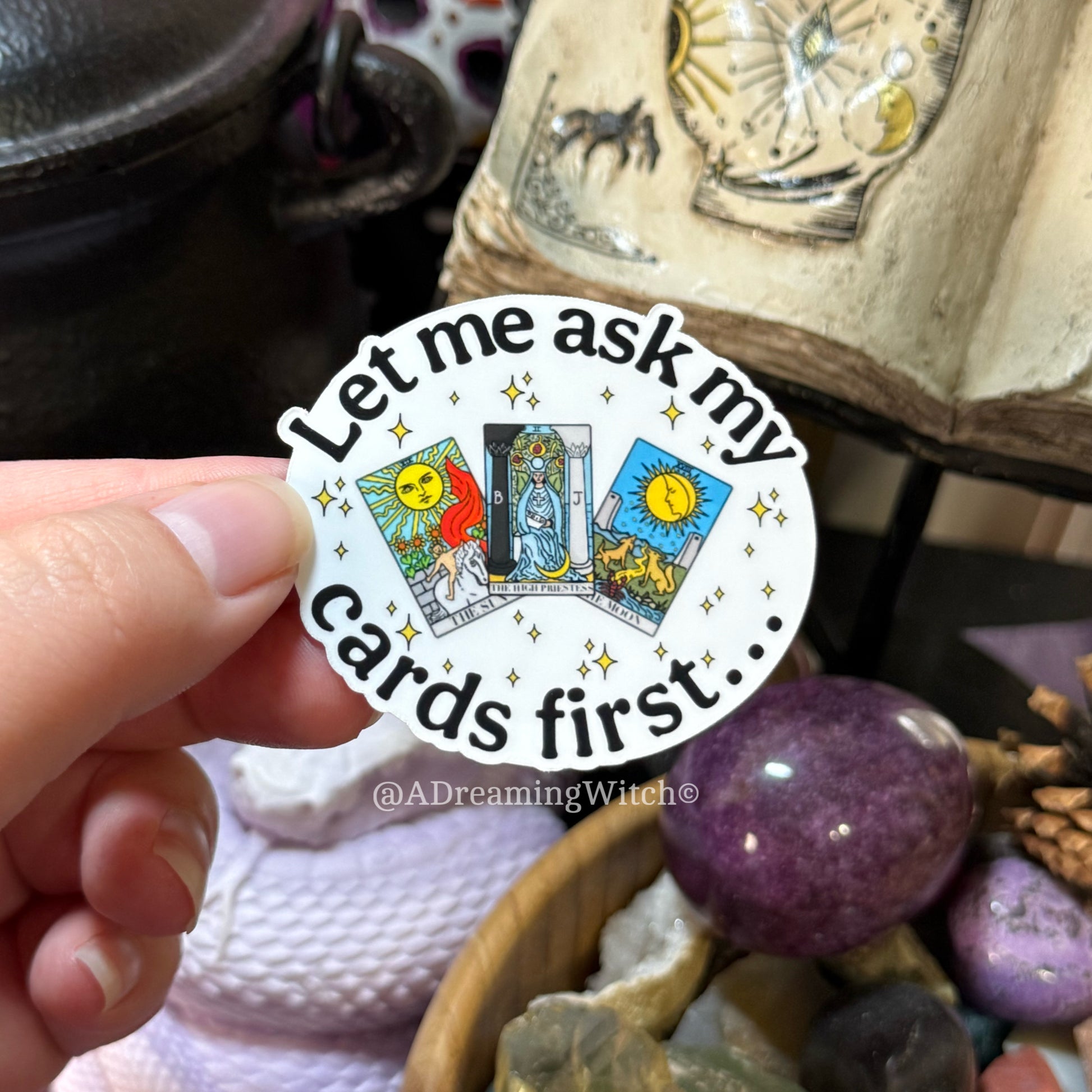Sticker with tarot card design held by a hand, surrounded by mystical items.