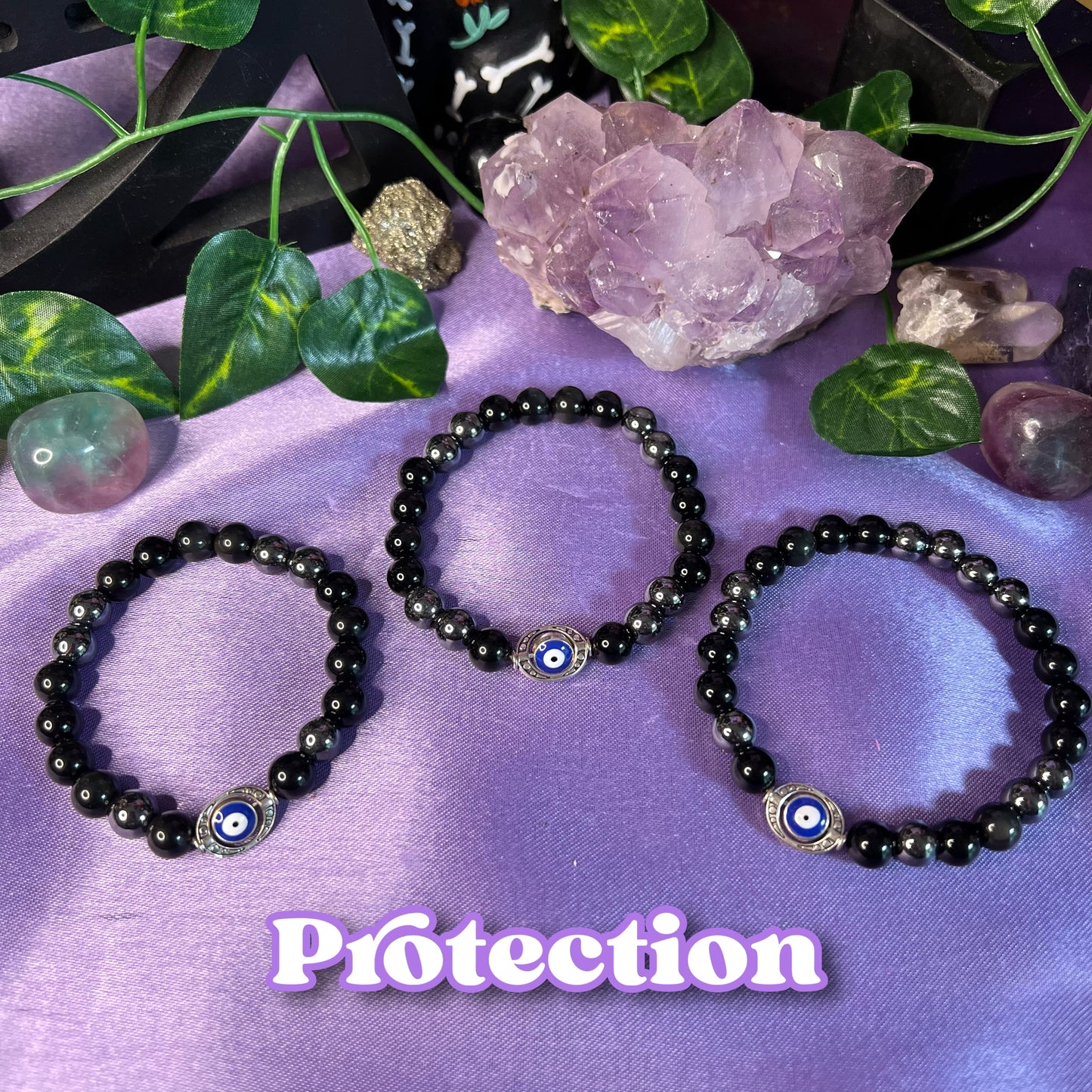 Three black bracelets with different designs, placed on a purple background with a crystal and a leaf, indicating they are protective bracelets with metaphysical properties.