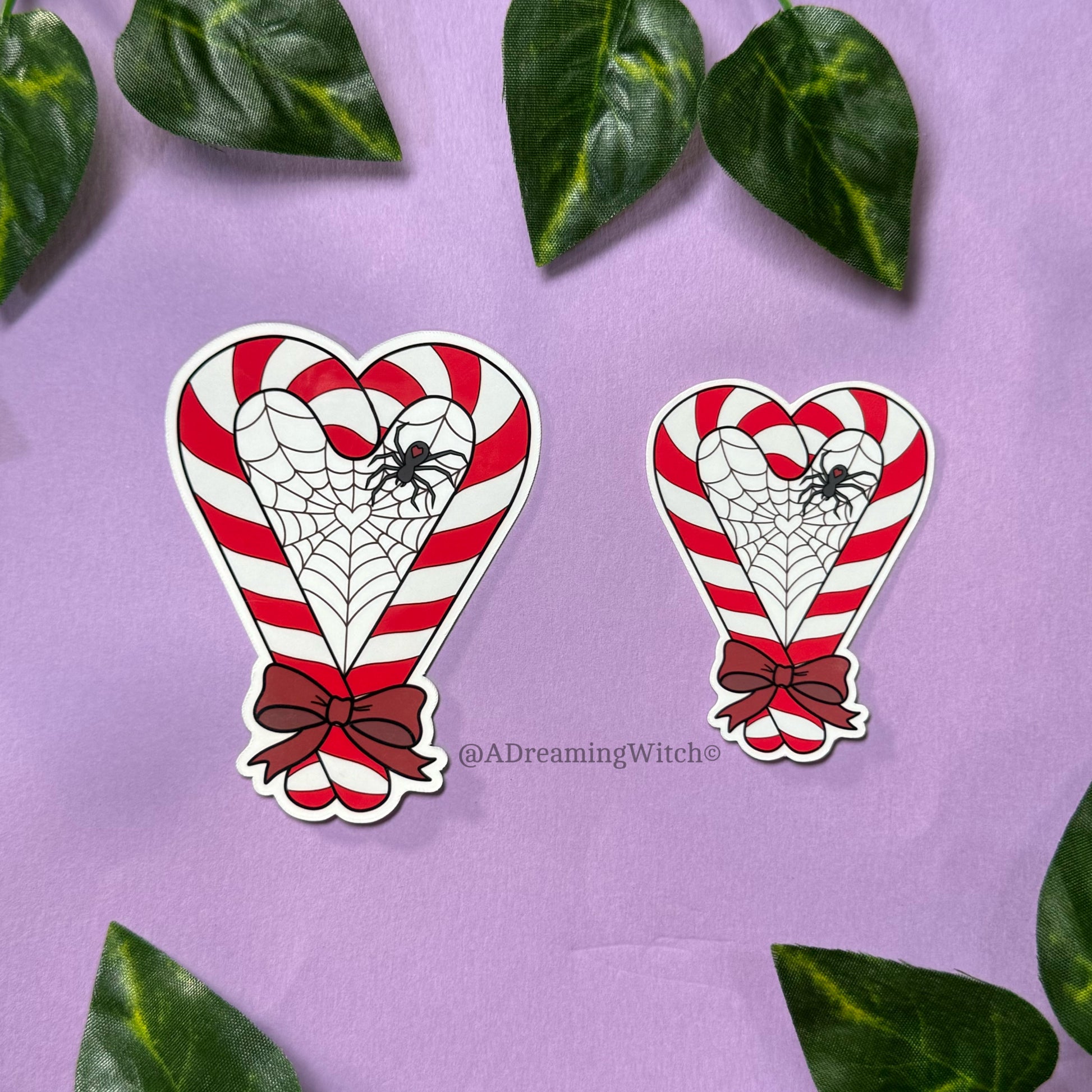 Two heart-shaped candy cane designs with spider webs and red bows on a purple background with green leaves.