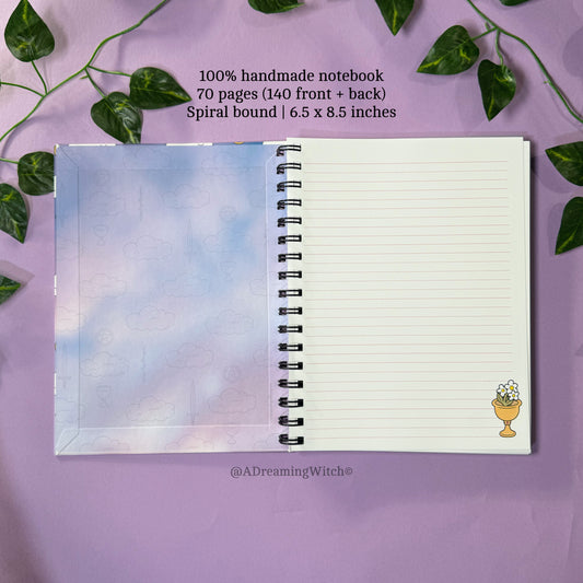 Handmade notebook with spiral binding on a purple background with green leaves.