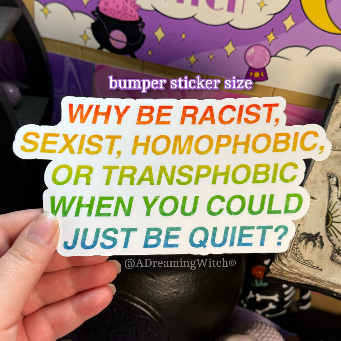 Sticker with anti-racism and anti-sexism message held by a hand, with a colorful background.